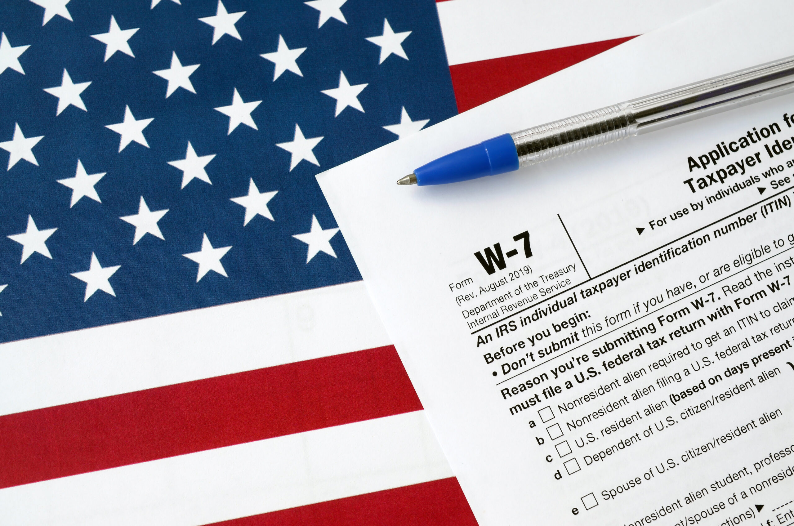 Form W-7 Application for IRS Individual taxpayer identification number and blue pen on United States flag. Internal revenue service tax form blank